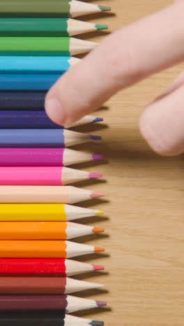 Vertical-Video-Of-Coloured-Pencils-Arranged-In-A-Line-On-Wooden-Background-With-Person-Choosing-Yellow-One